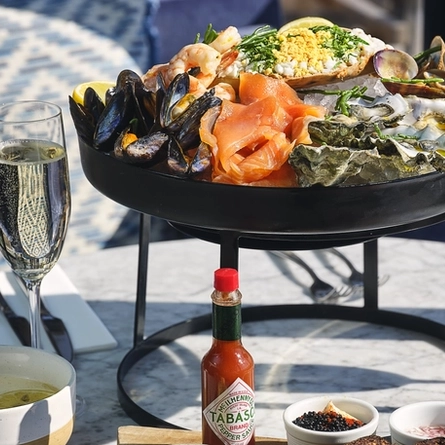An advertising image showing a Seafood Platter Sharing dish with a selection of accompaniments sat on an interior table with a glasses of sparkling white wine at The White Horses.