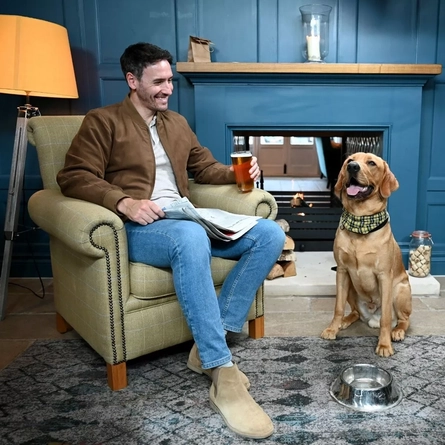 A man drinking a pint in the pub with his dog sat next to him