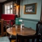 An interior restaurant seating area at The Ship; with an upholstered booth seat against the window, framed artwork on the walls, and wooden beams on the walls and ceiling.