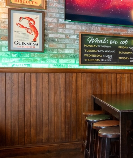 The bar and interior seating area of Molly Malones, with wooden furniture and TVs on the walls.