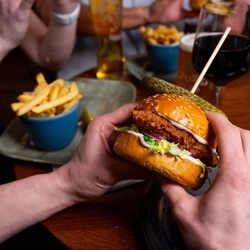 A focused image on a main burger meal served in the restaurant and seating area in a Urban Social venue with another burger meal blurred in the background and drinks served with the meals.
