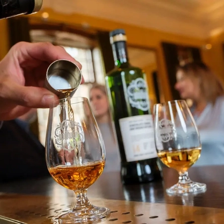 A hand pouring a dram of Whisky.