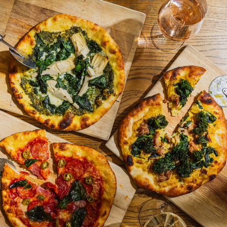 A lifestyle image showing 3 boarded Pizza dishes sat on a table within the interior restaurant seating area at The Four Oaks.