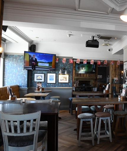 Interior dining area of a pub with a bar, a TV and a fireplace.