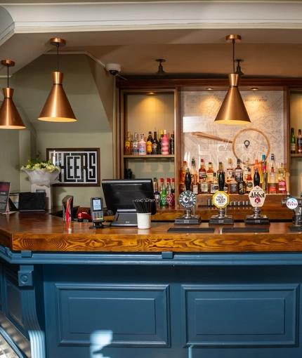 A close up view of the bar inside The Horsforth, with bottles of alcohol on wooden shelves behind the counter.