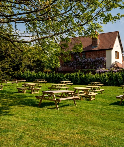 The exterior beer garden seating area at The Walkford in Walkford, with wooden picnic tables and trees on a large lawn.