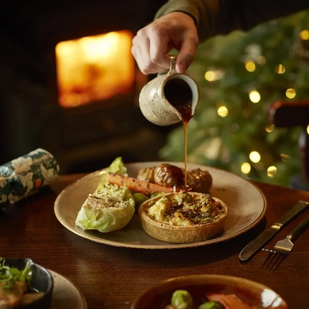 Gravy being poured onto a pie, served with vegetables and potatoes.