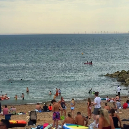 An image of a beach with a large amount of people sitting or swimming.
