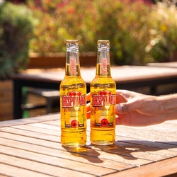 Two bottles of Desperados on an outdoor table, with a hand reaching for one of them.