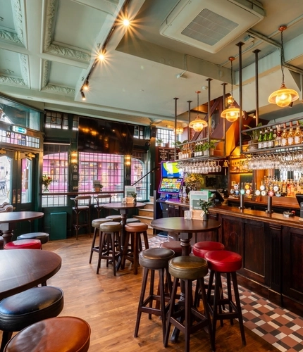 The bar and interior restaurant seating area at The Golden Lion in Soho, with a TV on the wall, a gaming machine, and glasses hanging in racks above the counter.