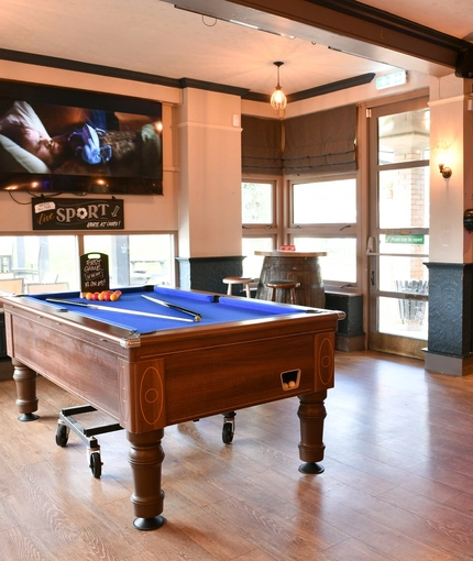 Interior seating area of a pub with a pool table, two gambling machines and a TV.