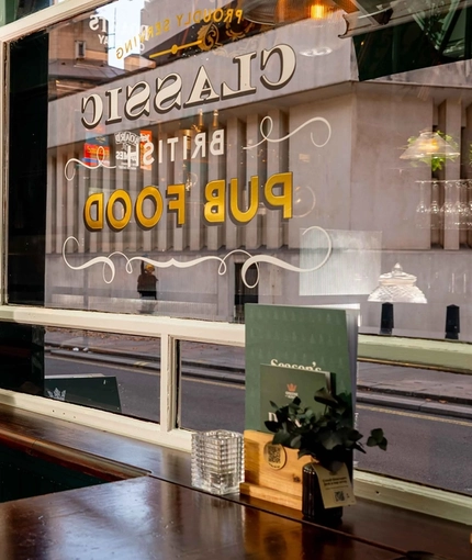 An interior restaurant seating area at Adam & Eve in St James, with a dartboard in the corner, and a TV on the wall above it.