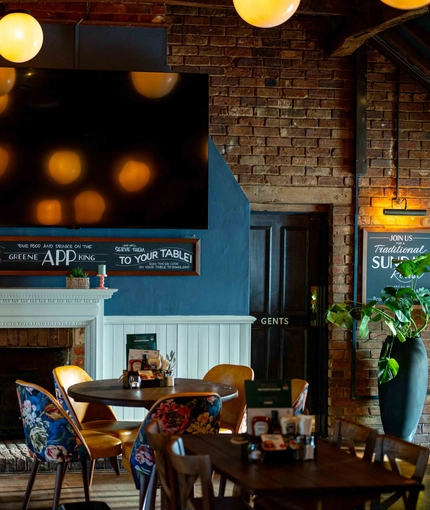 The interior restaurant seating area of The White Hart, with a TV on the wall, and a fireplace.