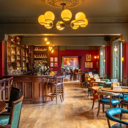 The wood panelled bar and interior restaurant seating area at The Beehive Inn, with upholstered chairs and bar stools, and framed artwork on the wall.