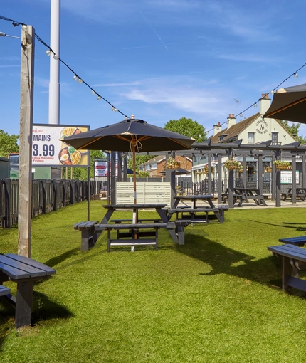 The exterior beer garden seating area with wooden tables and umbrellas, at The Good Intent in Hornchurch.
