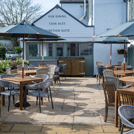 The paved exterior beer garden seating area at The Blue Cap in Sandiway, with wooden tables, planter boxes, and shade umbrellas.