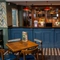 A close up view of the blue, wood panelled bar at the Devonshire Arms in Sheffield, with restaurant seating, checkerboard patterned floor, and bottles of wine and alcoholic spirits on wooden shelves behind the counter.