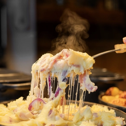A close up view of a large spoonful of cheesy onion mashed potato being lifted out of a large roasting dish.