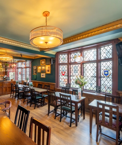 The interior restaurant seating area at The Golden Lion in Soho, with wood panelled walls, a small bar, golden cornices, and leaded windows with stained glass details.