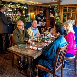 A mixed group of people sitting at an indoor wooden table that is festively decorated.