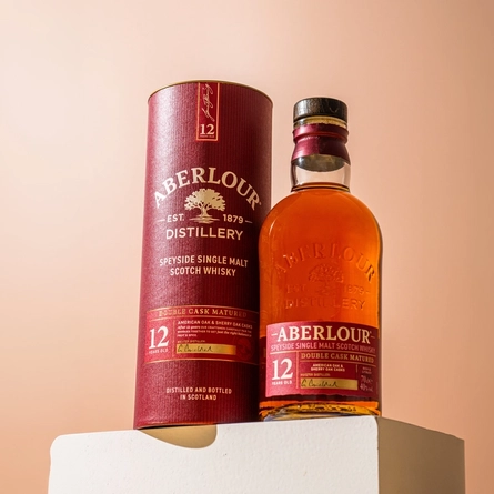 A close up view of a bottle of Aberlour Speyside Single Malt Scotch Whisky and it's presentation box, standing on a white box in front of a peach coloured background.