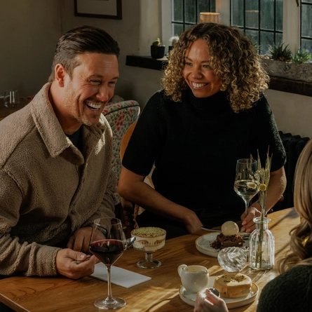An image focusing on 2 customers sat with friends enjoying desserts from the Prix Fixe menu sat at a table within the interior restaurant seating area of The Crown.