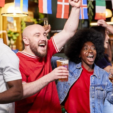 A mixed group of people holding a drink and cheering.