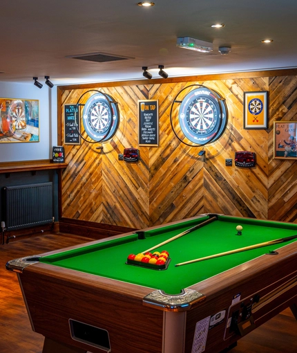 The interior games area at the Counting House in Dumbarton, with a pool table, two illuminated dartboards, and a TV on the wall.