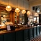 A close up view of the bar inside The Richmond Arms in Bournemouth, with spherical lights hanging above the counter; bottles of wine and alcoholic spirits on wooden shelves behind the bar; and a TV on the wall above.