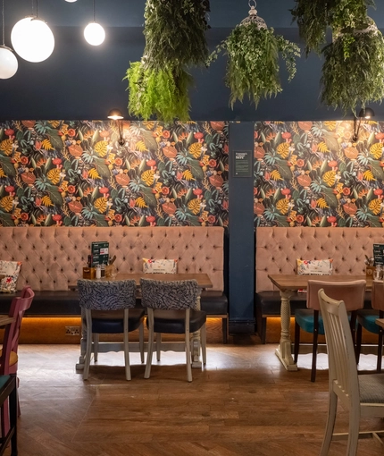 An interior restaurant seating area at The Royal Oak; with long, upholstered booth seats along one wall, and artificial flowers hanging on the walls and ceiling.