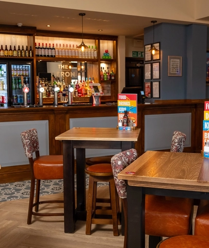 The bar and interior restaurant seating area at The Heron in Havant; with wooden tables, upholstered chairs, and bar stool seating.