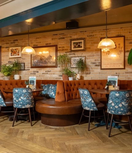 The interior restaurant seating area of the Cock & Pye, with upholstered booth seating and framed artwork on the wall.