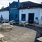 The exterior facade, signage, and paved beer garden seating area of The Kittoch in East Kilbride, with wooden picnic tables, and string lights overhead.
