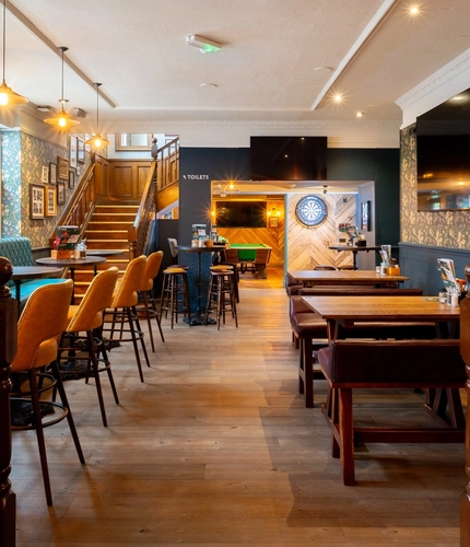 The interior restaurant seating area at The Talbot in Worcester; with a pool table, an illuminated dartboard, TVs on the walls, and a wooden staircase leading to the upper floor.