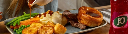 An image of gravy being poured over a Sunday Roast with a bottle of J20 within the interior restaurant and seating area at a Hungry Horse venue.