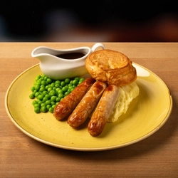 A plate of Sausage and Mash on a wooden table.