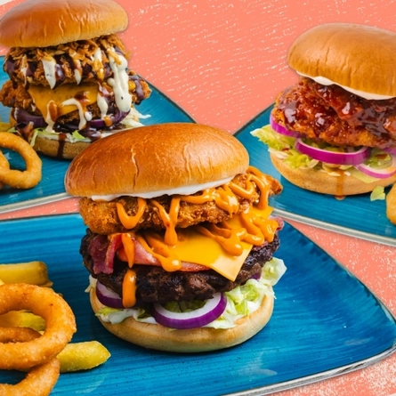 A main of burger fries and onion rings served to advertise burgers on offer at Flaming Grill venues on a textured pink background.