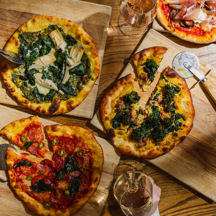 A lifestyle image showing 4 boarded Pizza dishes sat on a table within the interior restaurant seating area at The Four Oaks.