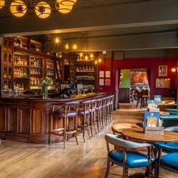 The wood panelled bar and interior restaurant seating area at The Beehive Inn, with upholstered chairs and bar stools, and framed artwork on the wall.