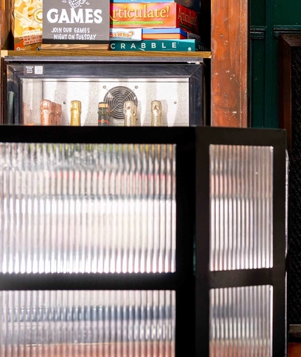 A close up view of the dartboard on the wall next to the bar inside Adam & Eve, with shots glasses sitting on the bar.