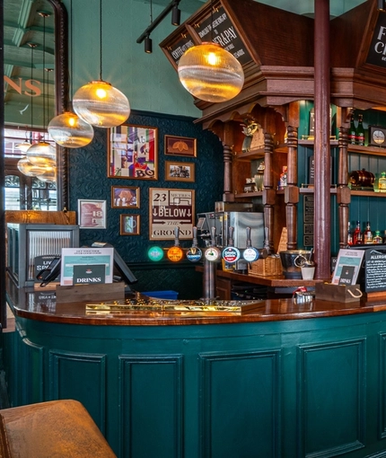 The wood panelled bar and interior restaurant seating area of The Fountains Abbey, with metal and wooden tables, upholstered seats, a TV on the wall and plants hanging above the bar.