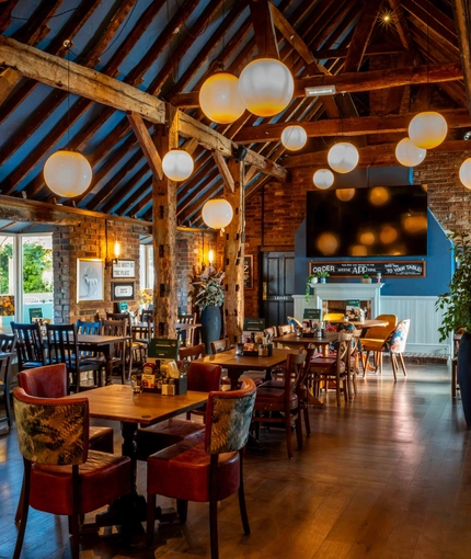 The interior restaurant seating area of The White Hart, with wooden beams, a TV on the wall, and a fireplace.
