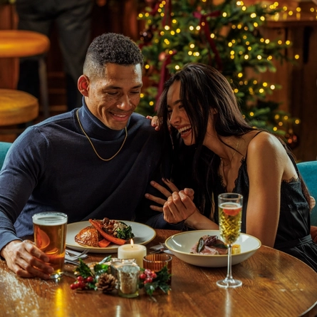 An image of 2 people enjoying various festive main dishes and drinks within the interior restaurant seating area during Christmas time at The Watermill.