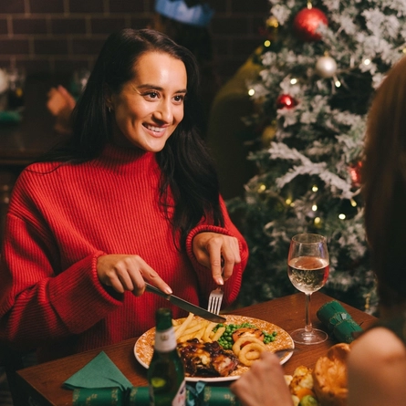 An image of 2 customers sat at a table enjoying festive main dishes and various drinks within the interior restaurant seating area at a Pub & Carvery venue.