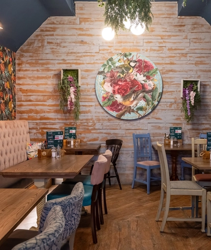 The interior restaurant seating area at The Royal Oak in Bishops Cleeve; with wooden flooring, an upholstered booth seat along one wall, and artificial flowers hanging on the wall and ceiling.