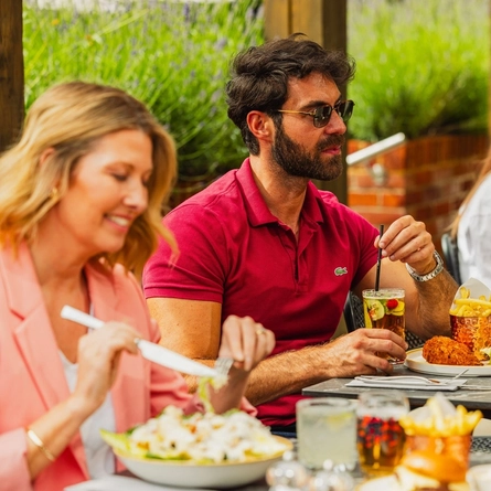 A group of people enjoying various dishes from the mains menu and drinks within the exterior beer garden seating area at a Crafted venue.