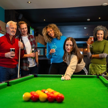 An image of a group of people enjoying drinks and a game of pool within a Flaming Grill venue.