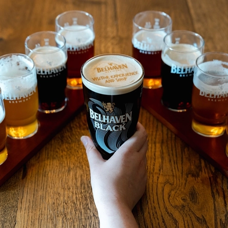 An image of a pint of Belhaven Black sat on an interior table with a detailed branded foam head design surrounded but several half pints of various Belhaven drinks at The Belhaven Brewery.