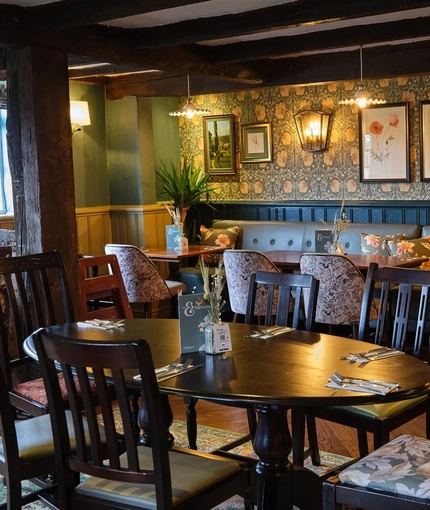 The interior restaurant seating area of the Smiths Arms pub, with wooden beams, upholstered booth seating, wooden tables, and framed artwork on the wall.