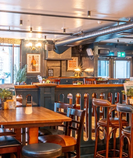 The interior restaurant seating area of the Monument, with wooden furniture and a TV on the wall.